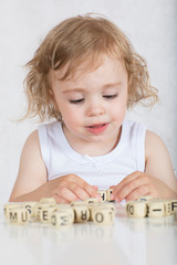Small girl composes words from letters. Closeup