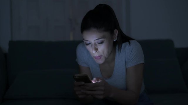 young attractive and relaxed hispanic 30s woman with mobile phone smiling happy using dating app late night in internet social media addiction concept
