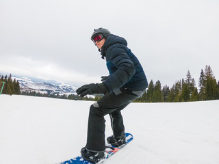 A young man in sports glasses is riding a snowboard in the mountains in Transcarpathia