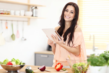 Happy woman preparing salad in modern kitchen and holding tablet