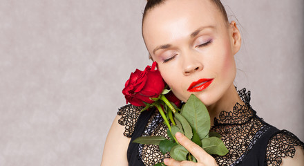 Young caucasian lady is posing in black blouse with red lipstick and red roses.
