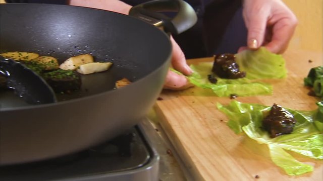 Woman rolling cabbages stuffed with black pudding and potatoes. The pan where it is cooking can be seen.