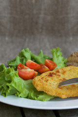 Chicken schnitzel with cherry tomatoes and green salad leaves.