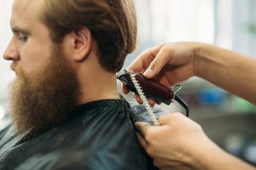 Bearded man having a haircut with a hair clippers. Closeup view with shallow depth of field