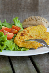 Chicken schnitzel with cherry tomatoes and green salad leaves.