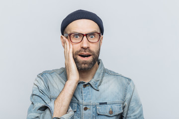 Portrait of amazed bearded excited male looks with surprisment in camera, recieves unexpected news, dressed in fashionable clothing, has attractive look, isolated over white studio background