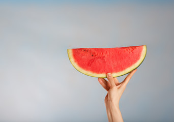 Young lady keeps a slice of water melon on a blue background.