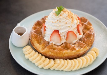 Delicious waffle with whipped cream and strawberry topping, eat with sliced bananas and honey. Focus on the sliced strawberry..