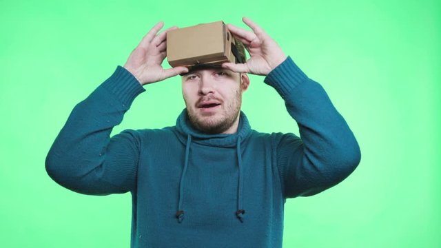 One funny male person use DIY emulator spectacles and joyful move in chromakey greenbox isolated closeup. Trendy guy leisure alone in vr-glasses connected to mobile with application. Freedom and joy
