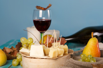 Cheese slices, pear, and grapes on a wooden stand.