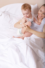 Young lady stays in the bed with her baby. Closeup