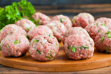 Raw meatballs on wooden cutting board and fresh parsley, close-up