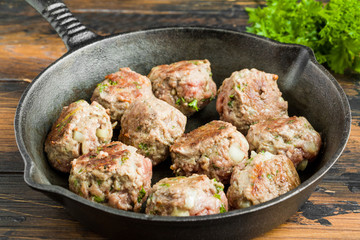Fried meatballs on black cast-iron pan on wooden table and fresh parsley, close-up