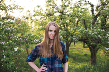 A young beautiful girl with long hair in a blue shirt in a cage into the blossoming apple tree. Spring
