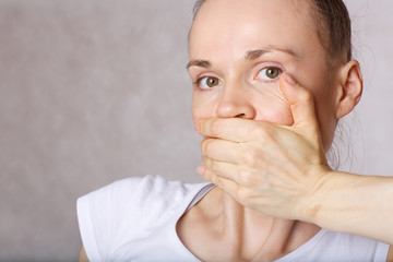 Mouth of young caucasian lady closed by another hand. Closeup