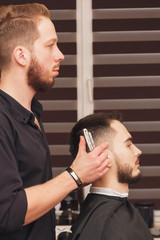 Shaving process at barbershop. Young bearded man getting haircut