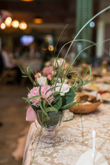 Close up rustic flower arrangement with beige flowers and a lot of greenery at a wedding banquet. Roses
