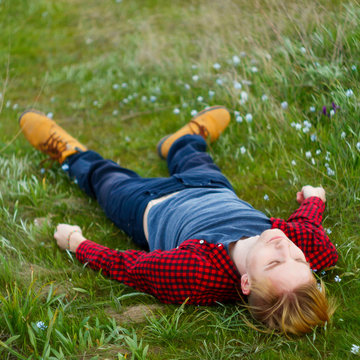 Picture of young beautiful blond man laying on green grass among small flowers. Spring wellness concept.