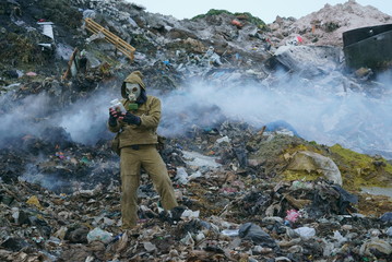 a man in a gas mask holds a sprout in the flask, against the background of fuming debris