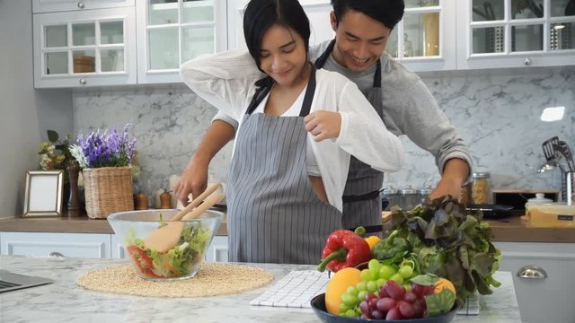 Young husband is wearing an apron for his pregnant wife in kitchen