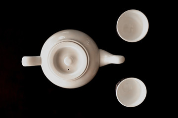 Teapot and two bowls on a black background. Traditional oriental tea drinking.