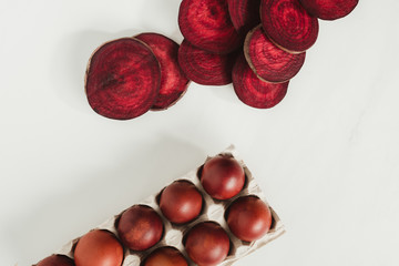 top view of painted chicken eggs in egg box and beetroot slices on grey