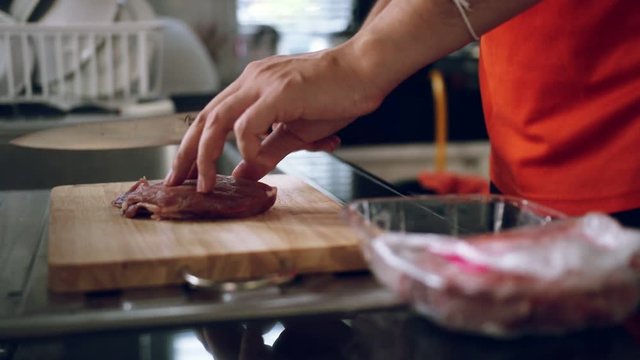 Female cuttiing raw meat with the knife on wooden board at home kitchen.