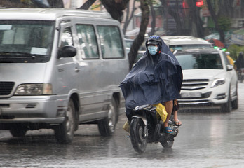 Fototapeta premium Ludzie w płaszczu przeciwdeszczowym jeżdżą na motocyklu w deszczu. Transport w mieście podczas deszczu.