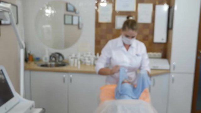 Blurred, defocused, blur video. Beauty clinic. Beautician in gloves making face aging injection in a female skin. face is being wraped by towel to warm up. Facial rejuvenation.. Shot in 4k