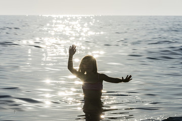 Little girl bathing in the sea surrounded by sunbeam reflections