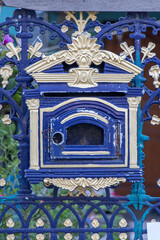 A old empty decorative mailbox on fence. Blue domestic post-box with ornaments on iron gate.