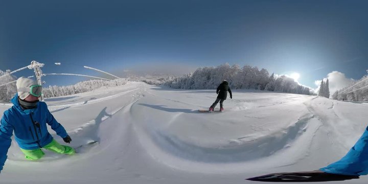360 VIRTUAL REALITY, LENS FLARE, SELFIE: Active freeriders riding down empty ski slope on fun winter vacation. Easygoing couple snowboarding in freshly fallen snow on a perfect day at the ski resort.