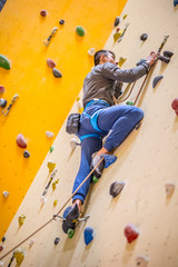 Climber on wall.Young man practicing rock climbing on a rock wall indoors - obrazy, fototapety, plakaty