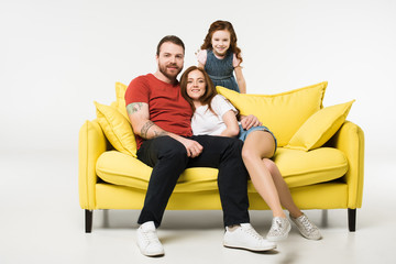 Couple sitting on couch with daughter behind isolated on white