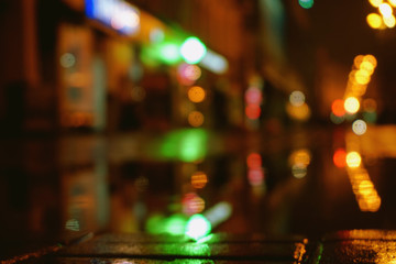 Night city lights bokeh from the shopping center, shop windows. Colorful surface of asphalt, blurred background. 