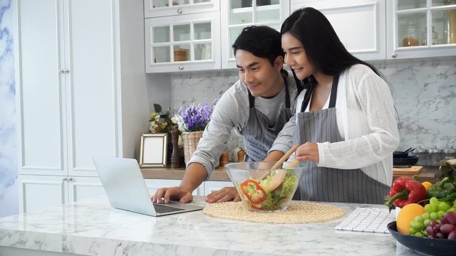 The happy spouses use laptop computer while cooking in kitchen