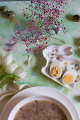 Polish traditional sour soup, zurek. Light background, eggs and tulips. White plate.
