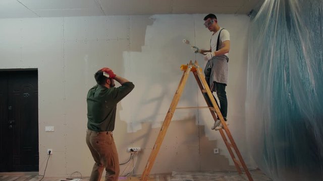 Angry house painter grasps his head, comes to the ladder, screams at his co-worker who throws the painting brush away, arguing. Conflict situation, having troubles. Slow motion, camera stabilizer shot
