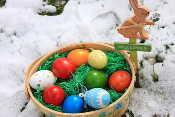 korb mit bunten ostereiern neben osterhase aus holz im garten mit schnee
