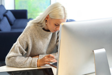 Praca na komputerze. Młoda kobieta siedzi przy stole w salonie i pracuje na laptopie  - obrazy, fototapety, plakaty