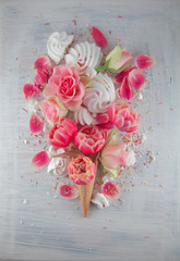 Flatlay waffle sweet ice cream cone with pink tulips and roses blossom flowers over white wood background, top view. Spring or summer mood concept.