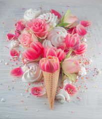 Flatlay waffle sweet ice cream cone with pink tulips and roses blossom flowers over white wood background, top view. Spring or summer mood concept.