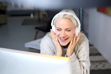 Kobieta z słuchawkami na uszach pracuje przy komputerze. - obrazy, fototapety, plakaty