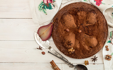 Chocolate cake with pears stewed in red wine, hazelnuts, walnuts on white wooden background. Traditional dessert. Top view.