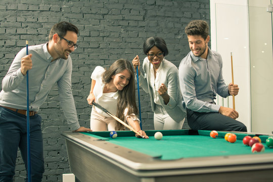 Young men and woman playing billiards at office after work.