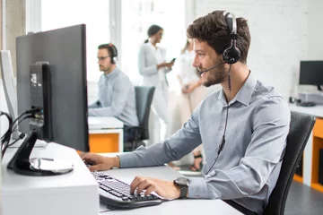 Deurstickers Smiling handsome customer support operator agent with hands-free device working in call center © Bojan