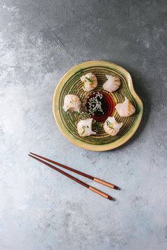 Asian steam potstickers dumplings stuffed by shrimps, served on ceramic plate with soy sesame sauce and chopsticks over grey texture background. Top view, space.