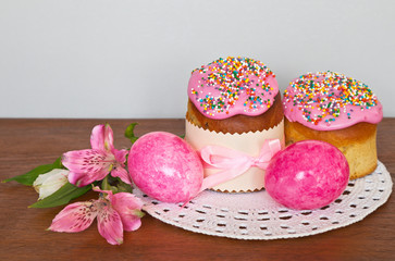 Traditional Easter food: home cakes with sweet icing and pink bright eggs on a lacy napkin. Easter still life. Empty space for text