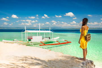 Young woman with yellow dress standing in the shade ona beach an