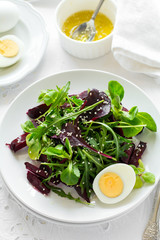 Fresh salad with beetroot, mix leaves, olive oil, egg and sesame seeds on white table cloth